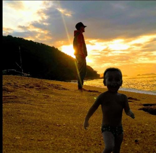a man and a child walking on the beach at Pousada Refugio Prumirim in Ubatuba