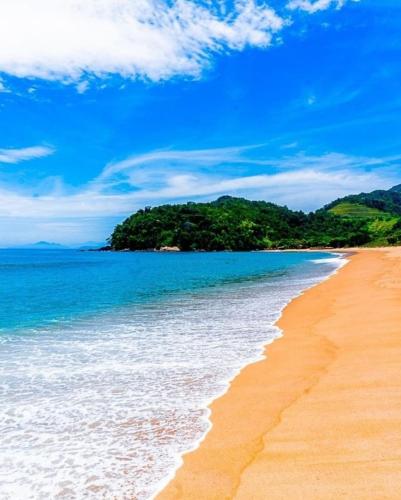 a sandy beach with blue water and trees in the background at Pousada Refugio Prumirim in Ubatuba