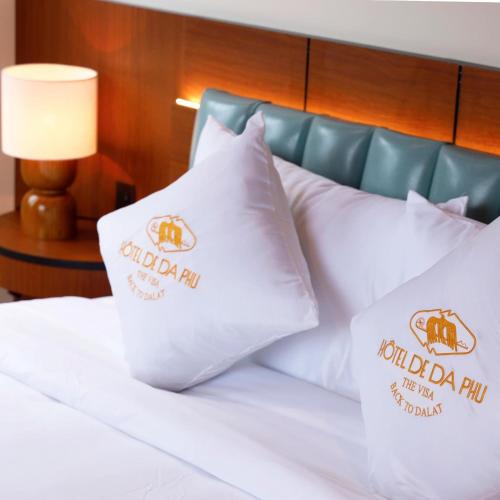 a bed with white pillows with the royal danish pin on them at Hôtel De Da Phu in Da Lat