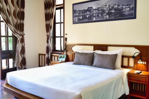 a bedroom with a large white bed with two windows at The Muse House in Hoi An