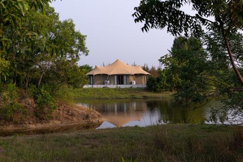a building with a thatched roof next to a pond at The Alampara Resort - Luxury Boutique Glamping & Water sports in Cheyūr