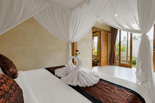 a bedroom with a large white bed with curtains at Pucuk Ubud Villa in Ubud