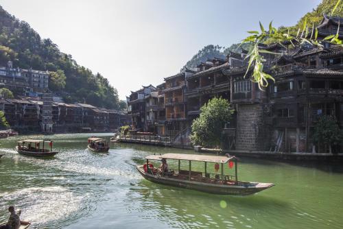 a group of boats on a river with buildings at Fenghuang Jiang'an Xinghe Hotel in Fenghuang
