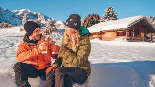 two people sitting in the snow in front of a cabin at Corona Dolomites Hotel in Andalo