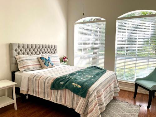 a bedroom with a bed and a chair and two windows at Custom luxury house in Katy near I10 and 99 in Katy