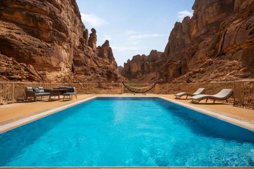 a pool in a canyon with chairs and a table at Shaden Resort in AlUla