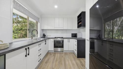 a kitchen with white cabinets and a large window at Boronia Oasis - Tranquil Oasis By The Creek, Sleeps 4 in Sawtell