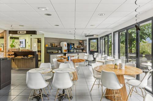 un restaurant avec des chaises blanches, des tables et des fenêtres dans l'établissement Hôtel AKENA La Ferté Bernard, à Cherré