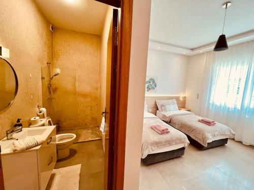 ein Schlafzimmer mit zwei Betten und ein Badezimmer mit Waschbecken in der Unterkunft Villa Petit Val d'Or - 3BR Comfort, and Beachside in Temara