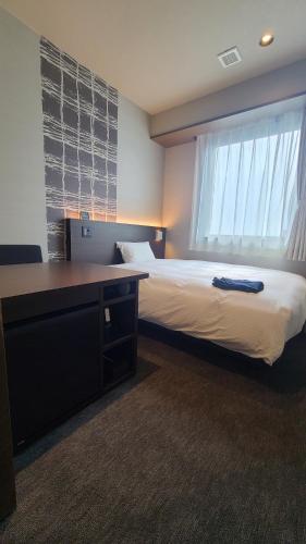 a bedroom with a bed with a desk and a window at 今治ステーションホテル in Imabari