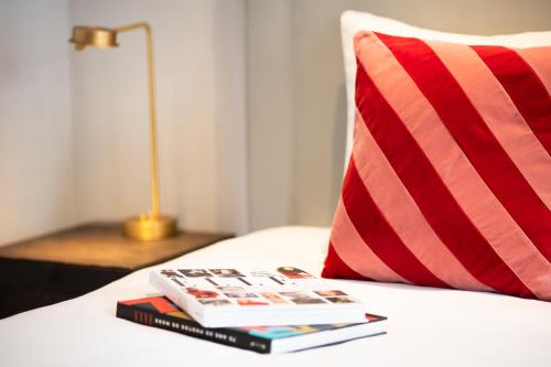 a stack of books on a bed next to a pillow at Maison ELLE Amsterdam in Amsterdam