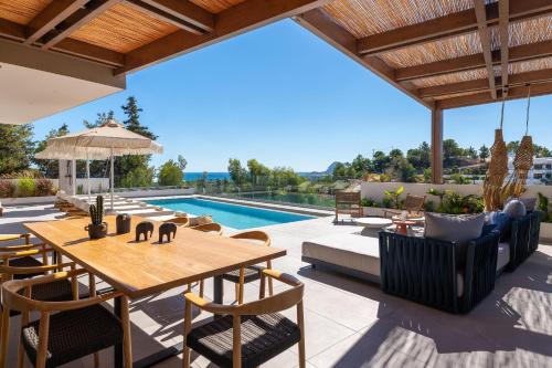 a patio with a wooden table and chairs and a pool at Mirena Luxury Living-Mirena Villa in Afantou