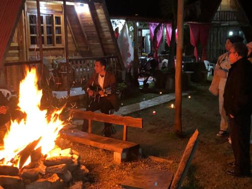 a man sitting on a bench next to a fire at Pousada e Camping Tio Wil in Extrema