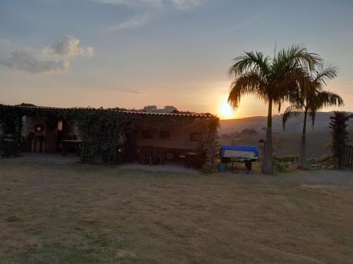 a house with a palm tree and the sunset at Pousada e Camping Tio Wil in Extrema