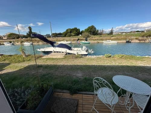 un patio avec deux tables et des chaises à côté de l'eau dans l'établissement La Villa Au Bord du Canal, à Frontignan