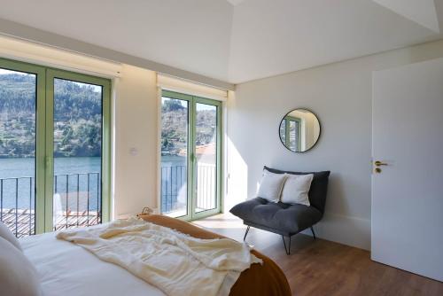 a bedroom with a bed and a chair and windows at Feel Discovery Casa de Cima Douro Valley in Riba Douro
