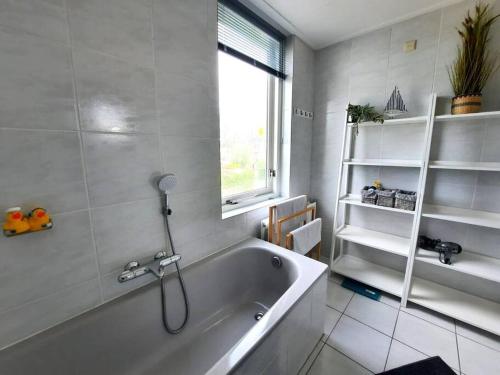 ein weißes Badezimmer mit Badewanne und Fenster in der Unterkunft Lamsoor 20 in Nieuwvliet