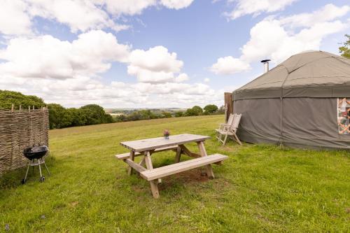 a picnic table and a tent in a field at Cosy-Hilltop-Yurt-StunningViews-Nature-HotTub in Cornworthy