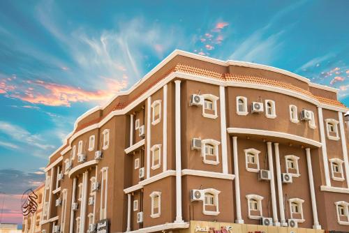 a brown building with white windows and a cloudy sky at SAHARI ALFORSAN HOTEL Sabya فندق صحاري الفرسان in Şabyā