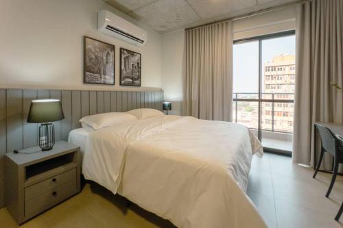 a bedroom with a white bed and a large window at Moderno e Central - CA905 in Maringá