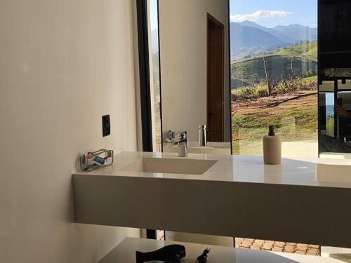 a white bathroom with a sink and a window at Solarium Mantiqueira 2 - Cinema e vistas incríveis in Itanhandu