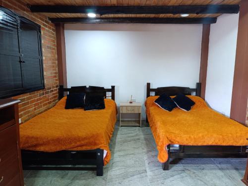 two beds with orange sheets in a room at Posada Rural - La Isabela in Tópaga