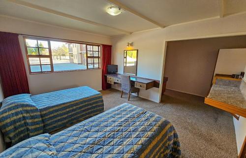 a hotel room with two beds and a desk and a mirror at Discovery Countrytime Hotel in Omarama