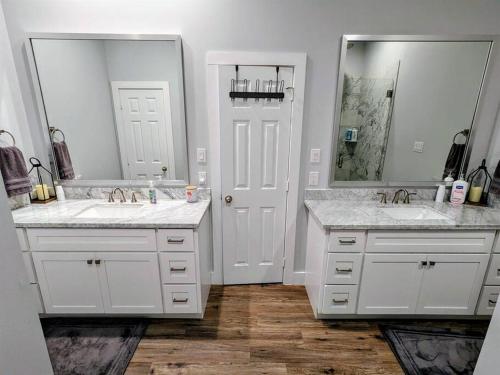 a white bathroom with two sinks and two mirrors at Tegarden Cottage at Gulfport Beach in Gulfport