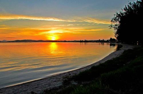 a sunset over a body of water with the sun setting at Casa perto da lagoa - Balneário São Pedro in São Pedro da Aldeia