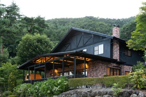 a house in the woods with a black roof at Kawaguchiko Country Cottage Ban in Fujikawaguchiko