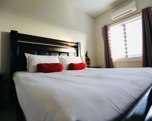 a bedroom with a white bed with red pillows at First home Fiji in Nadi