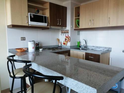 a kitchen with a counter and two stools in it at Departamento completo, centrico y estacionamiento in Temuco