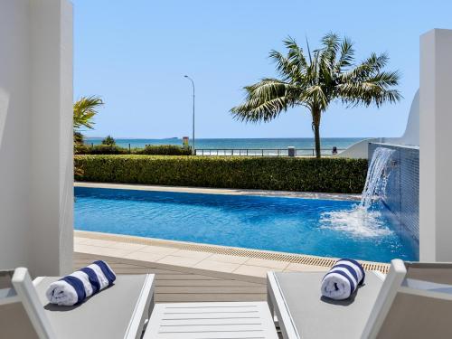 a swimming pool with two white chairs and a palm tree at The Beach House at Alex in Alexandra Headland