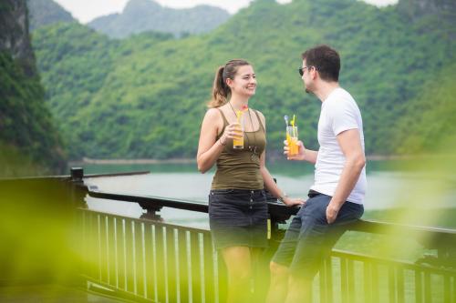 a man and a woman standing on a bridge with drinks at Majesty Luxury Prime Cruise by Premier Group in Ha Long