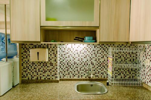 a kitchen with a sink and a tiled wall at Simply and Cozy Pool View 2BR at Great Western Apartment By Travelio in Pumpangsineng