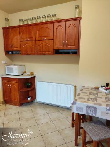 a kitchen with wooden cabinets and a table with a microwave at Jázmin Apartmanház in Szentgotthárd