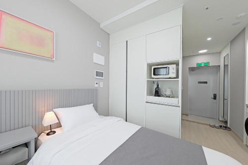 a white bedroom with a bed and a microwave at Elmomento Sasang in Busan
