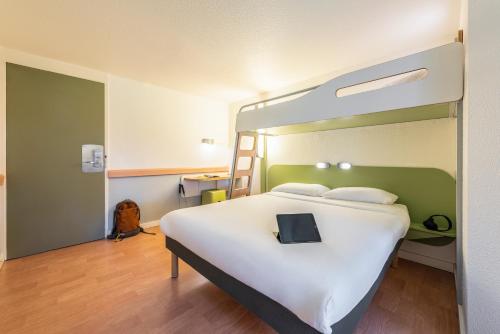 a bedroom with a large white bed with a laptop on it at Ibis Budget Villefranche in Limas