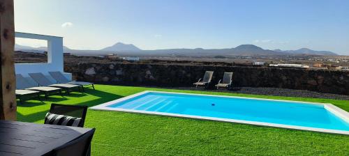 a swimming pool in a yard with grass and chairs at Villa Los Volcanes in Lajares