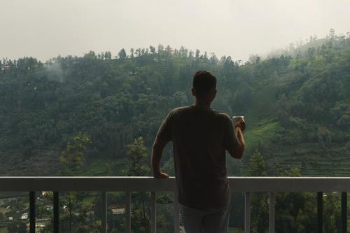 a man standing on a balcony taking a picture of the mountains at Heath Cote in Ooty