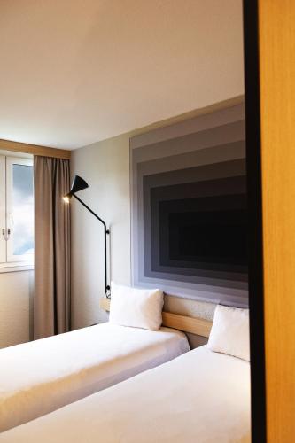 two beds in a hotel room with a tv on the wall at ibis Le Mans Est Pontlieue in Le Mans