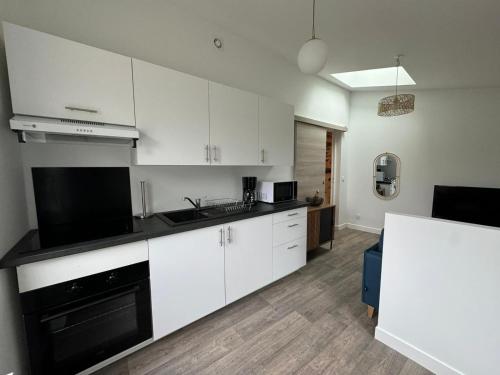 une cuisine avec des armoires blanches et un appareil noir dans l'établissement Le Glanois, calme et paisible, à Saint-Junien