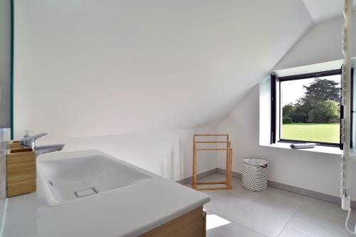a white bathroom with a sink and a window at Kertromel - Grande maison pour 10 in Saint-Lormel
