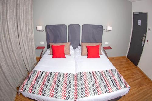 a large bed with two red pillows on it at Hôtel Méditerranée in Calvi