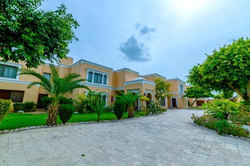 a large yellow house with trees and a driveway at Hotel One Bahawalpur in Bahawalpur