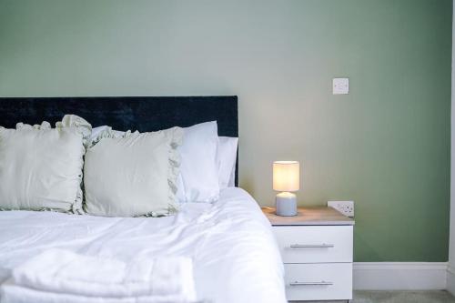 a bed with white sheets and a nightstand with a lamp at Sleeps 6, Stylish Apartment, Perfect For Groups, Long Term Disc in Otley