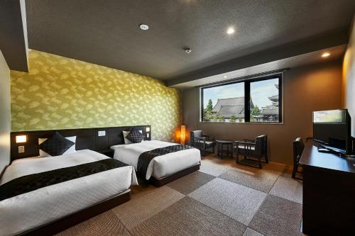 a bedroom with two beds and a desk and a window at Hotel Kuu Kyoto in Kyoto
