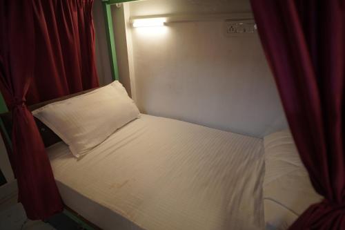 a small bed with a pillow in a room with red curtains at Hostel Funky Bunky in Udaipur