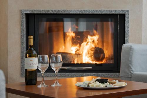 a bottle of wine and two wine glasses on a table with a fireplace at Alkyon Resort Hotel & Spa in Vrahati