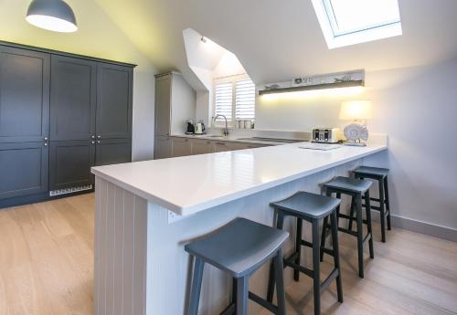 a kitchen with a large white counter and stools at Seashells Bracklesham Bay in Chichester